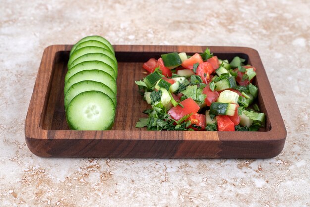 Een houten bord van gemengde groentesalade en gehakte komkommer.
