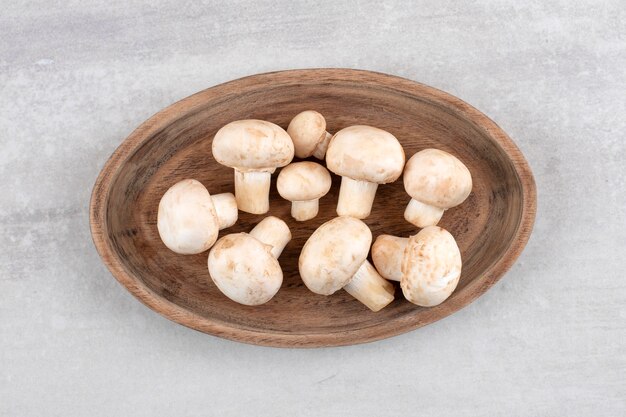 Een houten bord van verse witte champignons op stenen oppervlak.