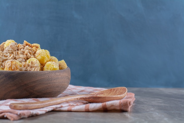 Een houten kom met gezonde cornflakes en een lege houten lepel.