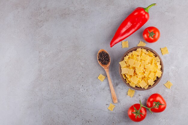 Een houten kom vol met ongekookte ravioli pasta met rode verse tomaten en chili peper.