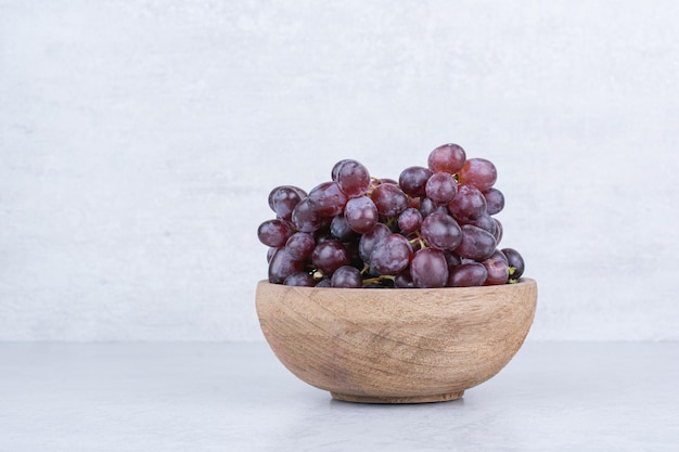 Een houten kom vol paarse druiven op wit