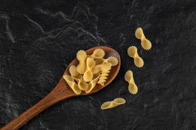 Een houten lepel vol rauwe farfalle tonde macaroni.