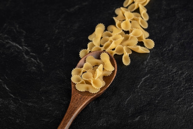 Een houten lepel vol rauwe farfalle tonde pasta.