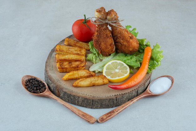 Een houten plaat met gebakken cgicken en groenten op marmeren tafel.
