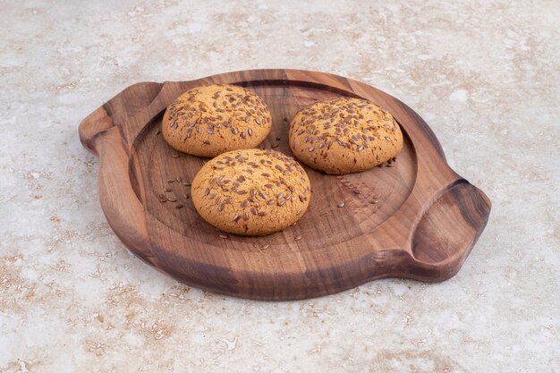 Een houten plaat van heerlijke koekjes met zaden op een stenen tafel.