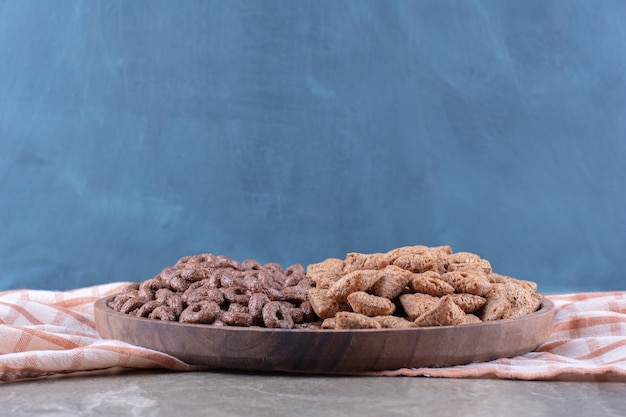 Een houten plank met gezonde chocoladegranenringen en cornflakes met chocoladepads.