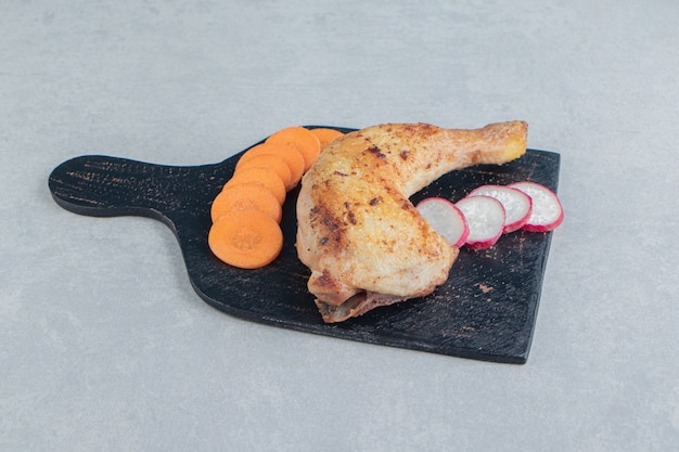 Een houten plank van kippenvlees met gesneden wortel en radijs.