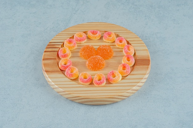 Een houten plank vol ronde sinaasappelgeleisnoepjes in de vorm van ringen en oranje geleisuikergoed met suiker