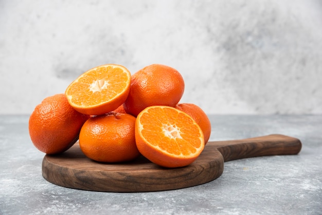 Een houten plank vol sappig oranje fruit met plakjes op stenen tafel.