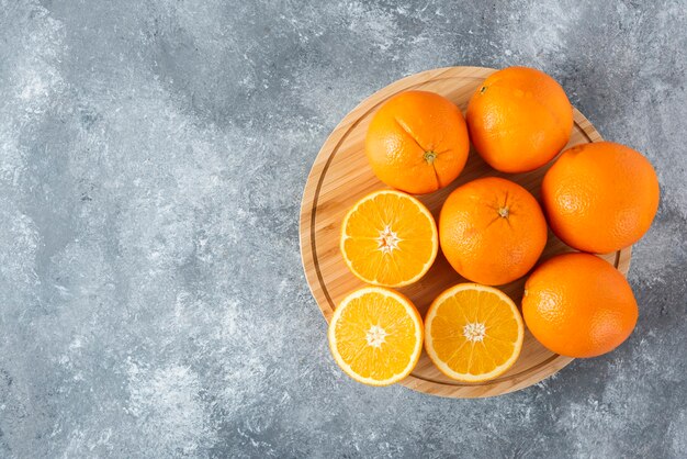 Een houten plank vol sappige plakjes oranje fruit op stenen tafel.