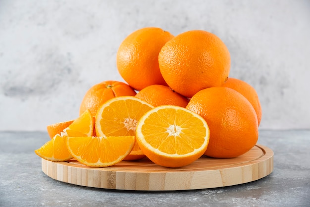 Een houten plank vol sappige plakjes oranje fruit op stenen tafel.