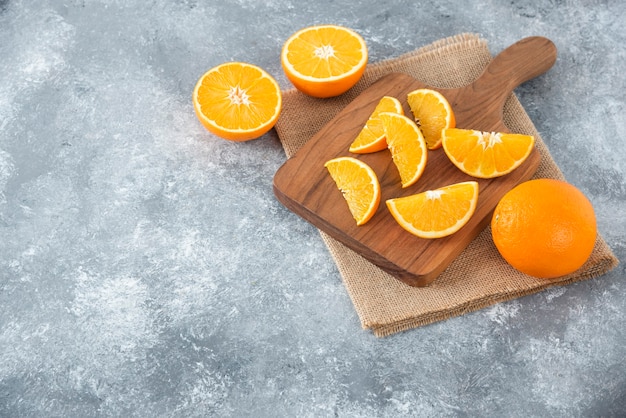Een houten plank vol sappige plakjes oranje fruit op stenen tafel.