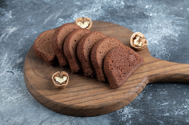 Een houten snijplank met sneetjes brood en walnoten.