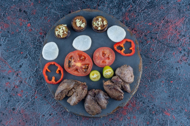 Een houten stuk kip schnitzels met een plakje tomaat.