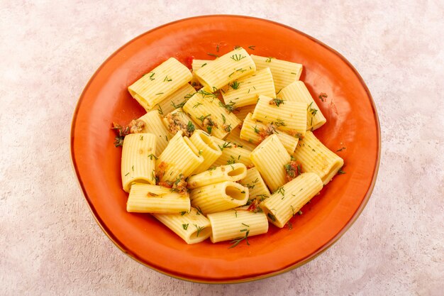 Een Italiaanse pasta van bovenaanzicht, smakelijk gekookt met gedroogde greens en gezouten binnen ronde oranje plaat op roze bureau