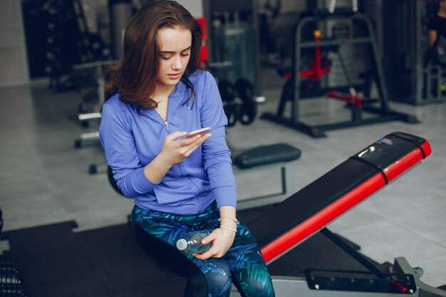 Een jong en mooi meisje, zittend in een sportschool met telefoon en water