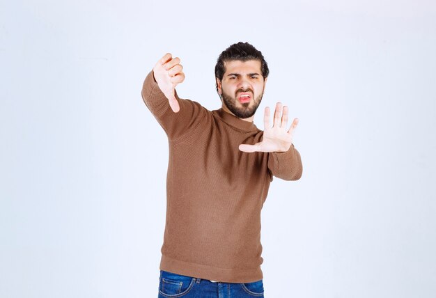 Een jong mannelijk model in bruine sweater die zich over witte muur bevindt.