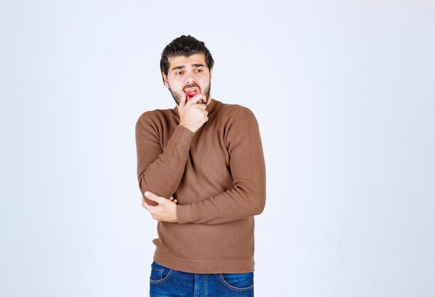 Een jong mannelijk model in bruine sweater die zich over witte muur bevindt.