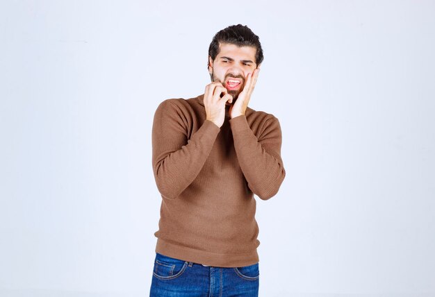 Een jong mannelijk model in bruine sweater die zich over witte muur bevindt.