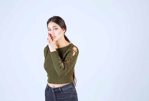 Een jong model in groene blouse vertelt geheim over witte muur