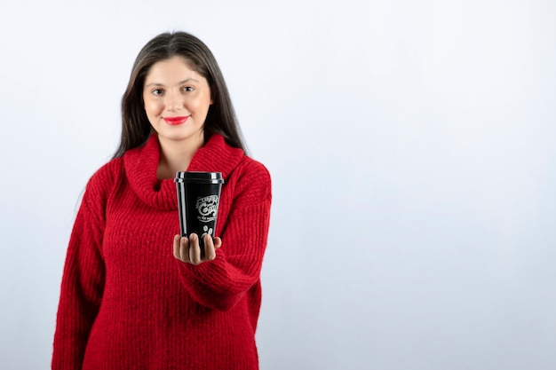 Een jong vrouwenmodel in rode sweater die een kop koffie aanbiedt