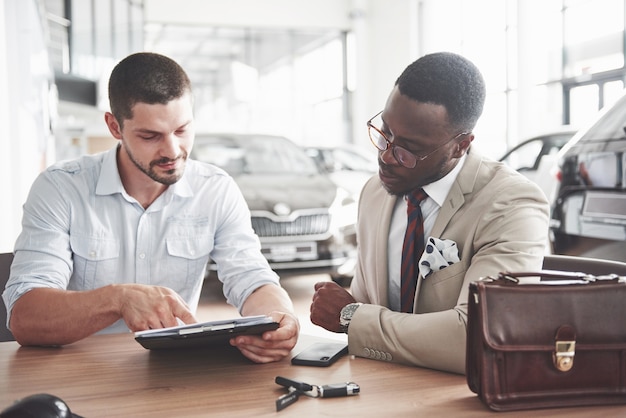 Een jonge aantrekkelijke zwarte zakenman koopt een nieuwe auto, hij tekent een contract en brengt de sleutels naar de manager.