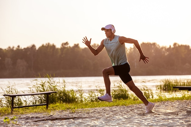 Een jonge atletische man traint het luisteren naar de muziek aan de rivier buiten