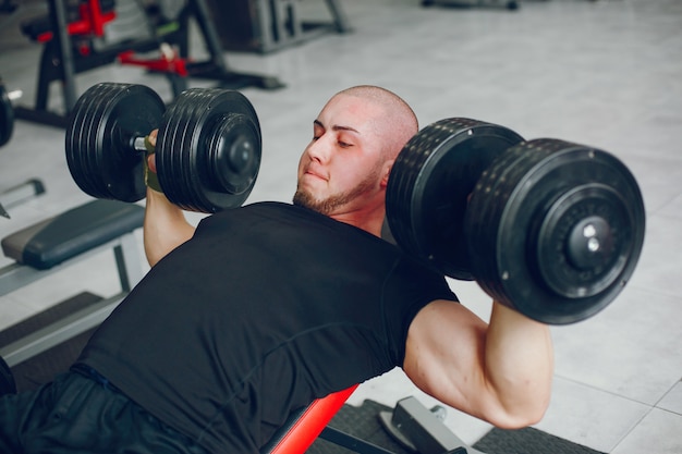 Een jonge en gespierde man in een zwart t-shirt traint in een sportschool