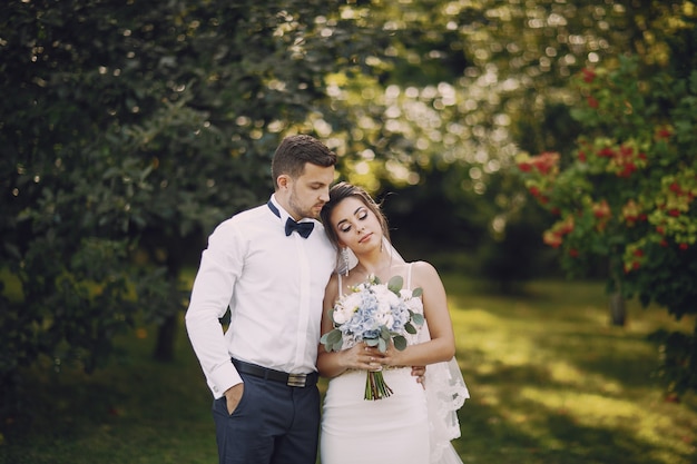 Een jonge en mooie bruid en haar echtgenoot die zich in een de zomerpark bevinden met boeket