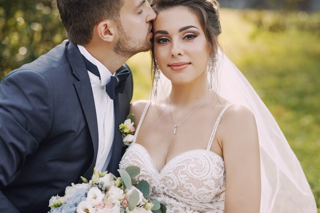 Een jonge en mooie bruid en haar echtgenoot die zich in park met boeket van bloemen bevinden