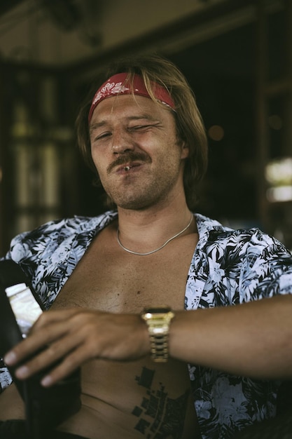 Een jonge knappe hippieman in een rode bandana met een blote torso rolt een tabakssigaret in een café op Bali.