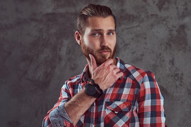 Een jonge knappe roodharige model man in een flanellen shirt op een grijze achtergrond.