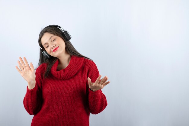 Een jonge lachende vrouw in een rode warme trui die muziek luistert in een koptelefoon