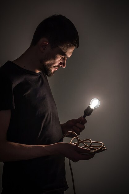 een jonge man die een brandende gloeilamp in de hand houdt op zwarte achtergrondconceptenideeën