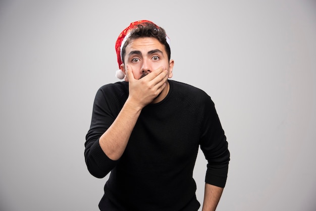 Een jonge man in de rode hoed van de Kerstman die zijn mond behandelt met hand.