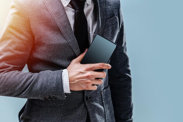 Een jonge man in een pak houdt een telefoon vast. de close-up van het lege scherm op een blauwe achtergrond