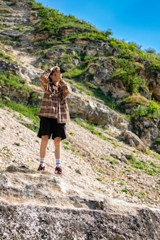 Een jonge man met krullend haar die foto's maakt met een camera in de natuur, terwijl hij op de helling van een rotsachtige heuvel blijft