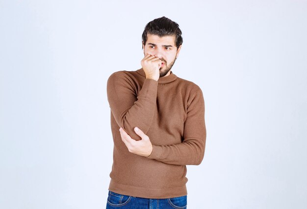 Een jonge man model staan en zijn nagels bijten over witte muur.