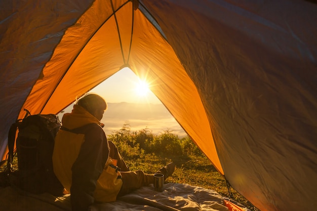 Een jonge man zit in de tent, kijkend naar het berglandschap in de winter