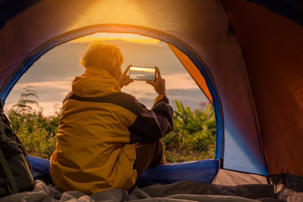 Een jonge man zit in de tent met het nemen van foto met een mobiele telefoon
