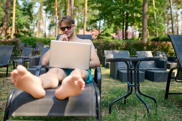 Gratis foto een jonge man zit op een chaise longue met een laptop