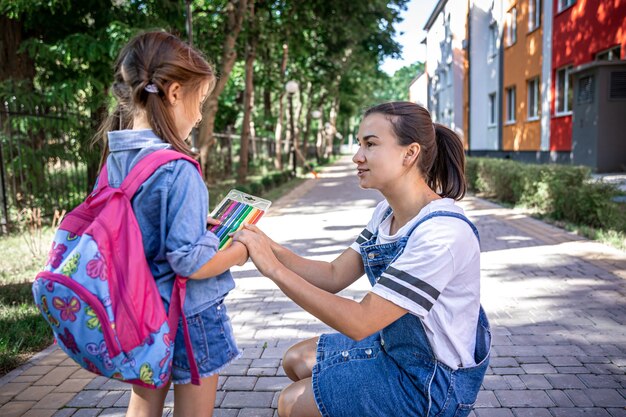 Een jonge moeder ziet haar dochtertje naar school gaan en geeft ze gekleurde stiften.