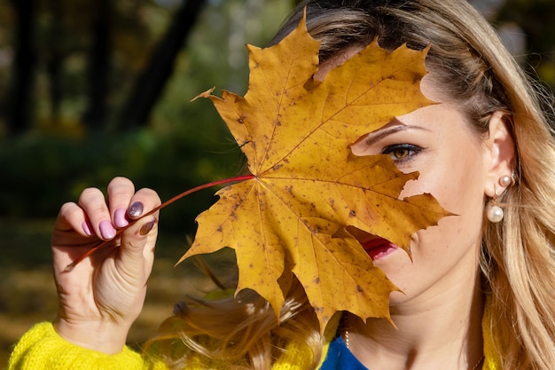 Een jonge mooie blonde vrouw die door het de herfstpark loopt en zich in kleurrijke boombladeren verheugt.