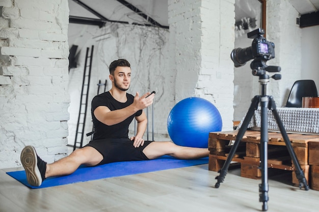 Een jonge, mooie fitnessblogger schrijft video's voor zijn blog en vertelt de basisregels tijdens een training, in een kamer in loftstijl