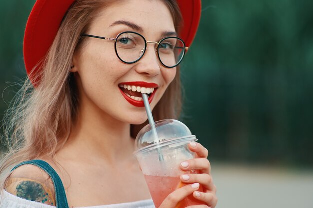Een jonge stijlvolle vrouw met een drankje tijdens het kijken naar de camera