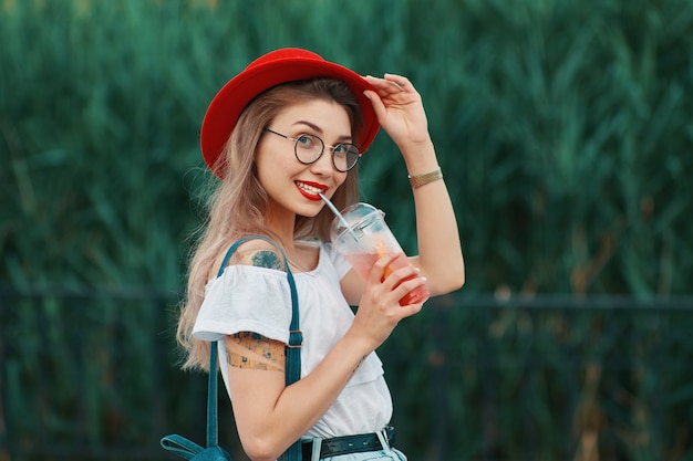 Een jonge stijlvolle vrouw met een verfrissend drankje tijdens het lopen