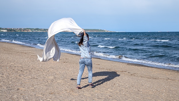 Een jonge vrouw aan zee heeft plezier met het vasthouden van een groot laken in de wind, een vrije levensstijl.