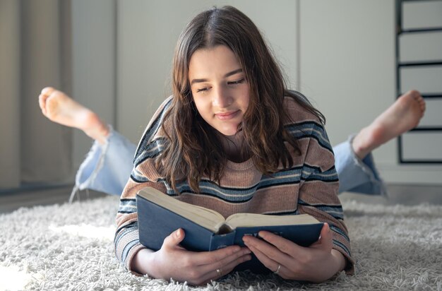 Een jonge vrouw die een boek leest terwijl ze thuis op de grond ligt