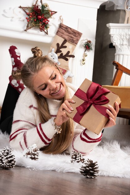 Een jonge vrouw die een kerstcadeau vasthoudt en op tapijt ligt.