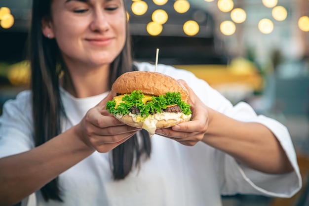 Gratis foto een jonge vrouw die hamburger eet in een straatcafé